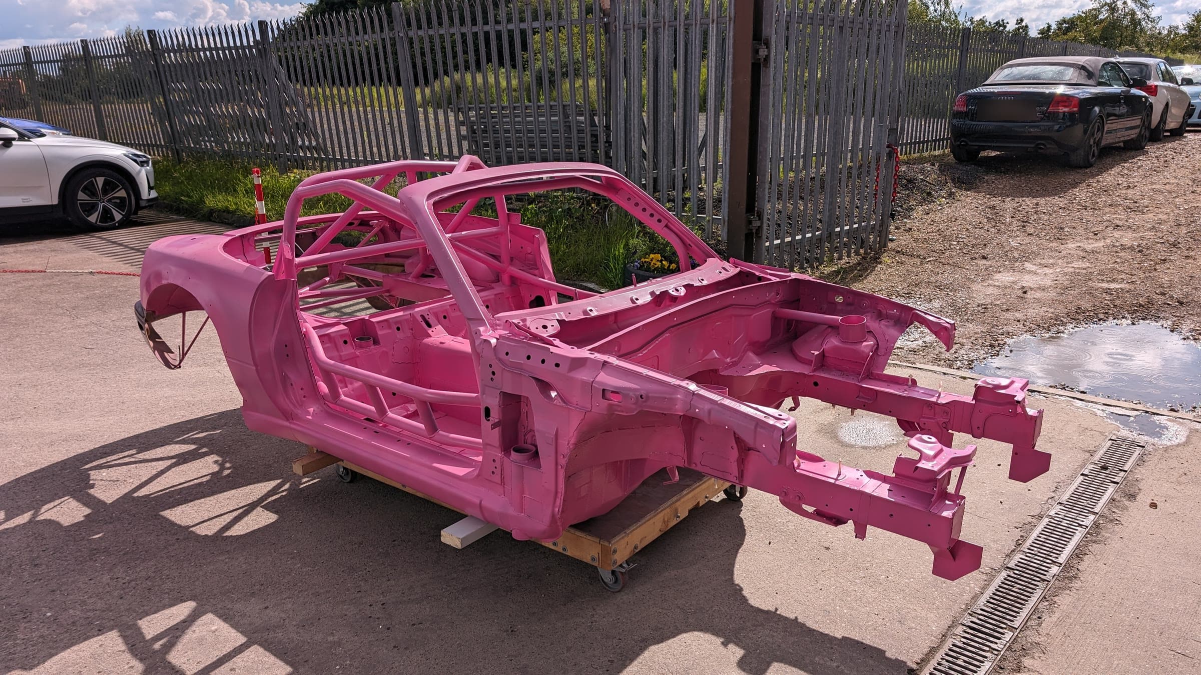 The bare MX5 race shell outside the workshop: full cage, seam-welded, front end stripped, no panels on